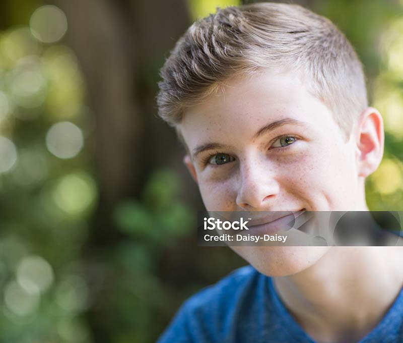 Portrait Of Happy Teenage Boy Sitting Outdoors